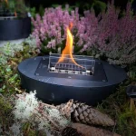 Tenderflame Carnation table top candle with black base on a table with foliage and pine cones