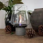 Tenderflame Amaryillis 25 table top candle in grey with real flame on a side board with pine cones