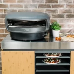 Everdure kiln pizza oven on on an outdoor kitchen unit with cooked pizzas