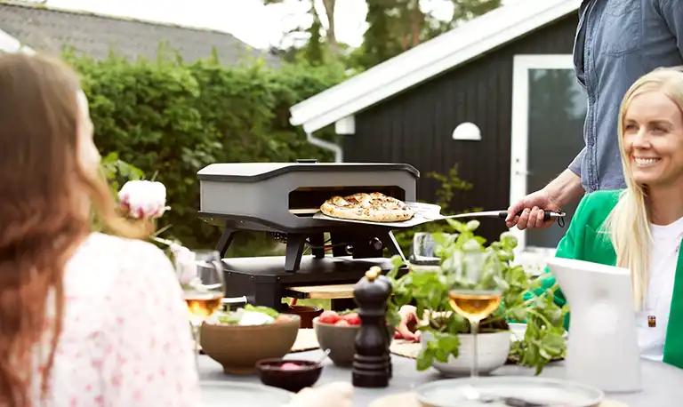 Cozze pizza oven being used to cook pizza by friends at a garden party.